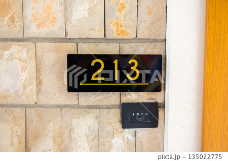 Apartment room 213 number sign on textured stone wall in corridor. Interior wayfinding, accommodation organization, architectural detail and functional navigation system for residential buildings 135022775