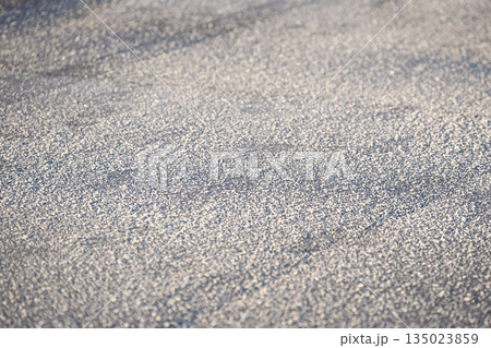 Deicing chemicals on asphalt in winter. Salt grains on icy sidewalk paving slab with technical salt 135023859