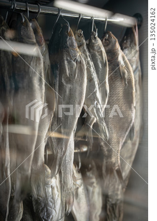 Dried fish hanging on hooks in a refrigerator at fishmonger, locals shop selling salted fish snacks. 135024162