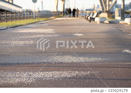 Deicing chemicals on asphalt in winter. Salt grains on icy sidewalk paving slab with technical salt 135024179