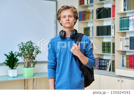Portrait of serious teenage student with backpack in classroom library 135024591