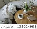 Cozy Scandinavian living room still life with coffee cup, books. Spring flowers, tulips and blooming cherry branches in vase on round wooden table. Elegant home interior lifestyle Easter morning scene 135024994