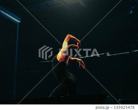 contemporary dancer on dark stage, striking spotlight silhouette conveying intense expression and fluid movement during latenight rehearsal, studio atmosphere with dramatic shadows and minimal props contemporary dancer on dark stage, striking spotlight silhouette conveying intense expression and fluid movement during latenight rehearsal, studio atmosphere with dramatic shadows and minimal props 135025478