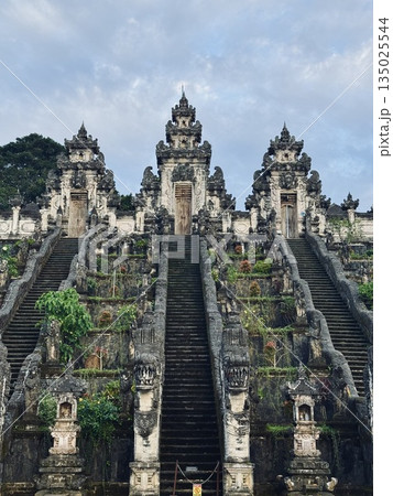 The gate overlooking the volcano of Pura Penataran Agung Lempuyang is a Balinese Hindu temple in Bali, Indonesia. ornate gateways frame mossy steps, lush hillside adorned with weathered shrines 135025544