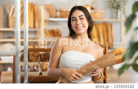 Positive young girl holding baguettes in paper bag Positive young girl holding baguettes in paper bag 135026182