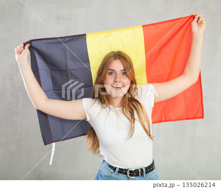 smiling girl in arms raised above head holds canvas of national flag of Belgium. 135026214