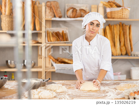 Young female baker kneading dough on table Young female baker kneading dough on table 135026219