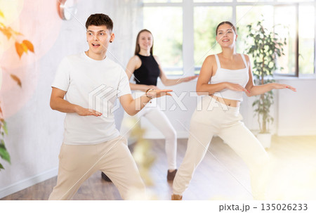 Girls and guys dancing synchronous group choreography in dance hall Girls and guys dancing synchronous group choreography in dance hall 135026233