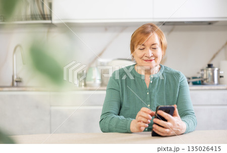 Positive mature woman writes a message to someone on a mobile 135026415