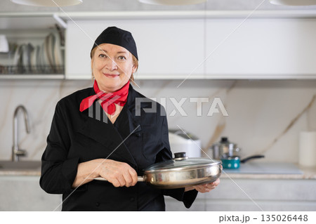 Adult woman in cook uniform posing with frying pan Adult woman in cook uniform posing with frying pan 135026448