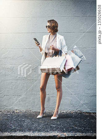 Shopping, outdoor and woman with a smartphone, retail and connection against a wall background. Female person, shopper or customer with bags, cellphone or boutique items with luxury, sale or discount 135026638