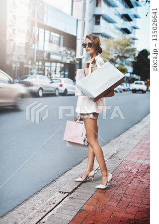 Travel, shopping bag and woman on street with fashion, retail and luxury promotion, sale or deal in urban city. Rich, wealth and young person or customer clothes, sunglasses and walking on sidewalk 135026641