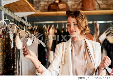 Retail, fashion and woman in a boutique, shopping and check price with discount, sale and clothes selection. Female person, customer or client buying outfit, choice and decision for items or products 135026647