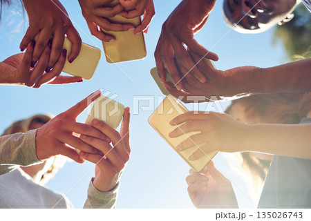 Hands, low angle and phone by friends together for social media, networking and sharing app on blue sky background. Below, smartphone and gen z people with internet, addiction or online communication 135026743