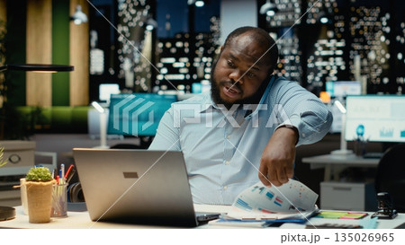 Male business director answers incoming phone call late at night, using laptop to read briefing data and engage in a transparent dialogue. Exchanges ideas to strengthen relations. Male business director answers incoming phone call late at night, using laptop to read briefing data and engage in a transparent dialogue. Exchanges ideas to strengthen relations. 135026965
