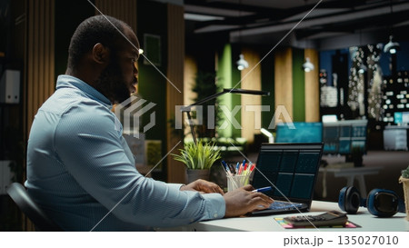 Black consultant reviewing data insights and managing agenda on laptop, drafting reports and proofreading to solve tasks. Notetaking supports goal setting for the business company. Black consultant reviewing data insights and managing agenda on laptop, drafting reports and proofreading to solve tasks. Notetaking supports goal setting for the business company. 135027010