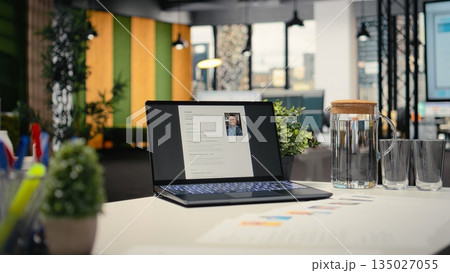 Modern desk with laptop in empty office shows applicant CV before hiring interview, office used for the recruitment process and reviewing qualifications or work experience to align with position. Modern desk with laptop in empty office shows applicant CV before hiring interview, office used for the recruitment process and reviewing qualifications or work experience to align with position. 135027055