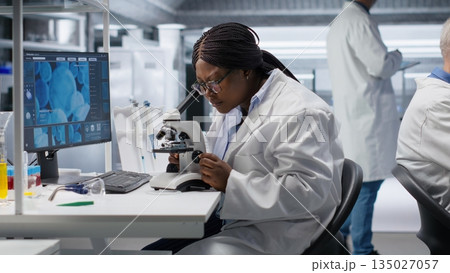 Black scientist examining samples under microscope in a modern laboratory. Research work integrates biotechnology, molecular science and advanced diagnostics to shape medical discovery. Black scientist examining samples under microscope in a modern laboratory. Research work integrates biotechnology, molecular science and advanced diagnostics to shape medical discovery. 135027057