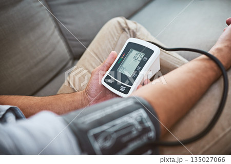 Hypertension, machine and person test blood pressure in a home sofa or living room for medical or health exam. Monitor, reading and man with closeup of equipment for chronic disease due to stress Hypertension, machine and person test blood pressure in a home sofa or living room for medical or health exam. Monitor, reading and man with closeup of equipment for chronic disease due to stress 135027066