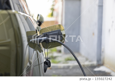Close up shot of plugged in electric vehicle equipped with rechargeable battery pack using renewable energy to be emission free. EV eco friendly car being charged while parked 135027242