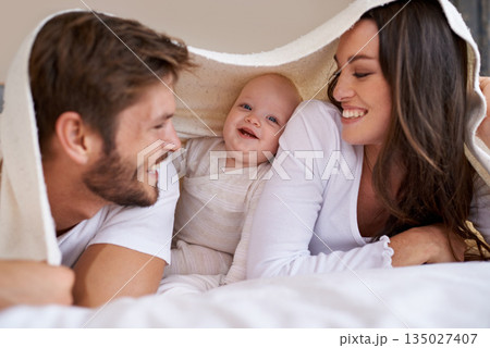 Happy mother, father and baby with blanket on bed for love, care and quality time together. Parents, family and playful newborn child relaxing in bedroom with bedding fort, smile and bonding at home 135027407