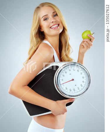 Woman in portrait, happy with apple and scale, lose weight and healthy food isolated on studio background. Female model with smile, health and diet with organic fruit with happiness and weightloss 135027612