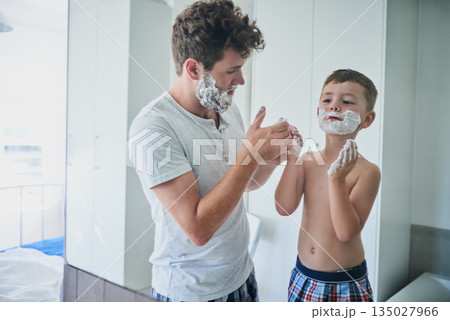 Father, kid and learning to shave in bathroom, education and bonding together. Care, dad and teaching child with shaving cream on face, playing or cleaning, hygiene or enjoying hair removal in home. Father, kid and learning to shave in bathroom, education and bonding together. Care, dad and teaching child with shaving cream on face, playing or cleaning, hygiene or enjoying hair removal in home. 135027966