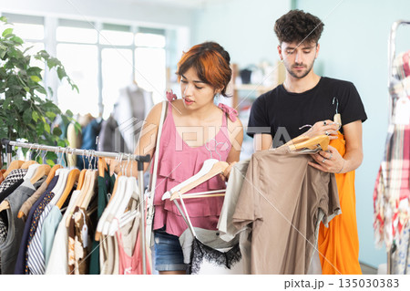 Young girl and guy browsing clothing racks in outlet Young girl and guy browsing clothing racks in outlet 135030383