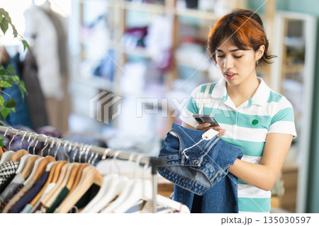 Female shopper checks quality of jeans by scanning QR code on label 135030597