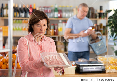 Woman chooses pork fillet, while her husband buys alcohol in supermarket Woman chooses pork fillet, while her husband buys alcohol in supermarket 135030645
