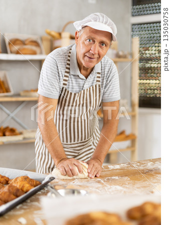 Senior man works in bakery as baker, kneads dough, works with flour. Senior man works in bakery as baker, kneads dough, works with flour. 135030758