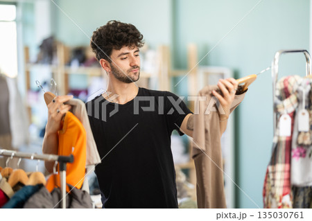 Young guy choosing t-shirt in clothing store Young guy choosing t-shirt in clothing store 135030761