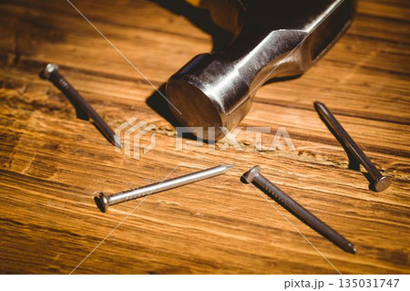 Flat design is showing metallic hammer head resting on warm wood surface with scattered steel nails Flat design is showing metallic hammer head resting on warm wood surface with scattered steel nails 135031747