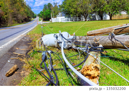 Fallen utility pole lies near rural road, with cables strewn on ground after bad tornado weather. 135032200