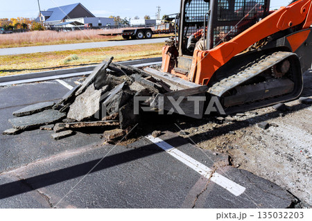 Construction equipment is actively lifting broken asphalt from parking lot, during repair work Construction equipment is actively lifting broken asphalt from parking lot, during repair work 135032203