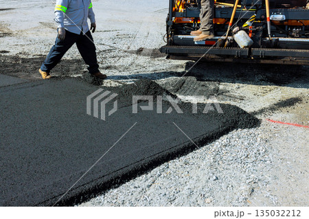 Workers operate paving machine spread asphalt during road construction in busy urban area. Workers operate paving machine spread asphalt during road construction in busy urban area. 135032212