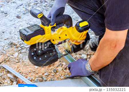 Worker operates cordless saw cutting tool on metal piping while on construction site 135032221