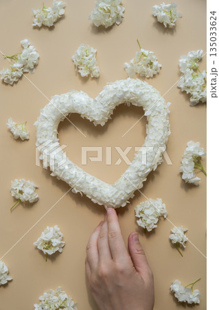 Female hand holding White lilac flowers heart shaped in pastel backdrop. Symbol of love floral arrangement. Spring concept idea Valentine's Day, weeding proposal postcard copy space Female hand holding White lilac flowers heart shaped in pastel backdrop. Symbol of love floral arrangement. Spring concept idea Valentine's Day, weeding proposal postcard copy space 135033624