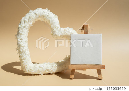 Heart made of white lilac flowers with white mock up paper template on pastel beige background. Still life romantic composition of Valentines day holiday copy space for your text invitation greeting 135033629