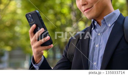 屋外でスマホを操作する笑顔のビジネスマン 屋外でスマホを操作する笑顔のビジネスマン 135033714