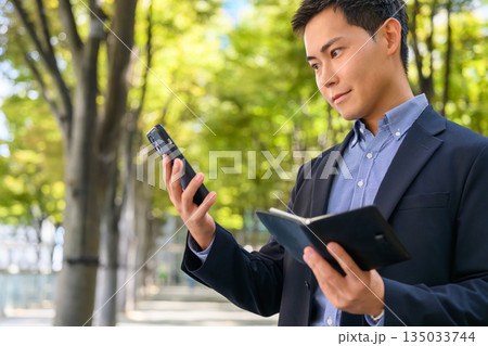 屋外で予定を確認するビジネスマン 屋外で予定を確認するビジネスマン 135033744