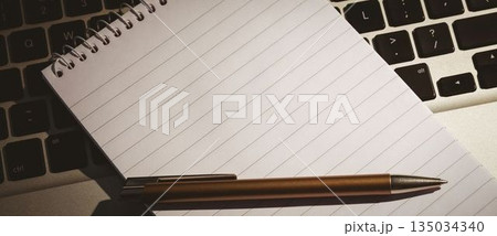 Spiral-bound lined notebook is resting diagonally on laptop keyboard in flat design with bronze pen 135034340