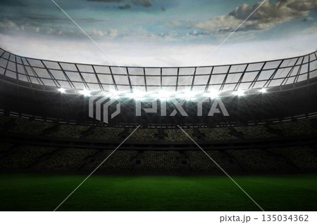 Empty stadium showing seating beneath metal roof, floodlighting green field under partly cloudy sky 135034362