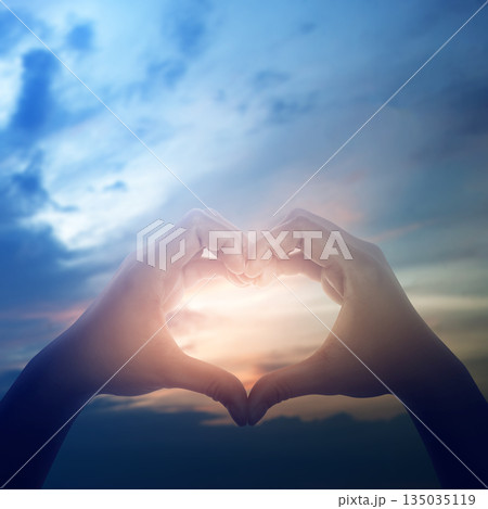 Two hands making a heart shape gesture against a beautiful sunset sky. Concept of love, hope, peace, faith, kindness, sharing, care, and support 135035119