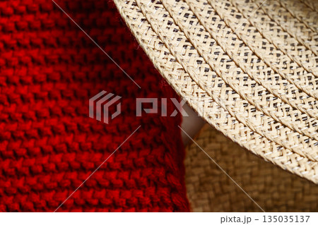 Closeup view showing the detail and texture of a woven straw hat and a red knitted fabric. The focus is on the intricate patterns and materials 135035137