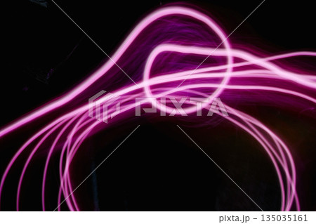Abstract image of pink neon light painting in a circular and spiral pattern against a black background. A modern and futuristic design element 135035161