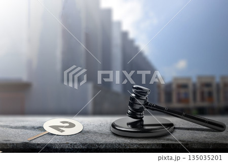 Gavel rests beside a numbered auction paddle on a textured table. City backdrop lends context to this scene, representing bidding and legal proceedings. Concept of auction 135035201