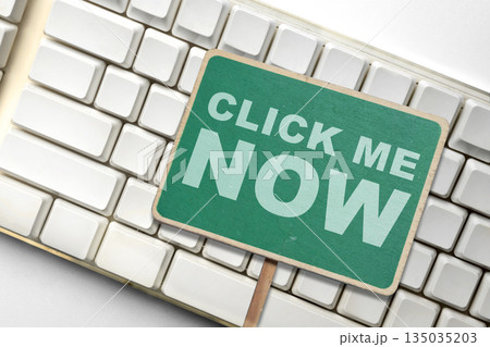 Closeup top view of a green sign with white text "Click Me Now" placed on top of a white computer keyboard. Concept of online action, call to action, and technology Closeup top view of a green sign with white text "Click Me Now" placed on top of a white computer keyboard. Concept of online action, call to action, and technology 135035203