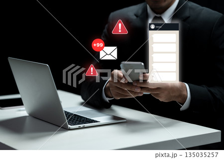 Businessman using a smartphone with a message notification and an email alert while working on a laptop. Concept of Scam Businessman using a smartphone with a message notification and an email alert while working on a laptop. Concept of Scam 135035257
