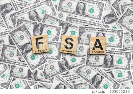 Wooden cubes spell out FSA with the words Flexible, Spending, and Account on them. The tiles are surrounded by a pile of US dollar bills. Concept of a Flexible Spending Account (FSA) Wooden cubes spell out FSA with the words Flexible, Spending, and Account on them. The tiles are surrounded by a pile of US dollar bills. Concept of a Flexible Spending Account (FSA) 135035259